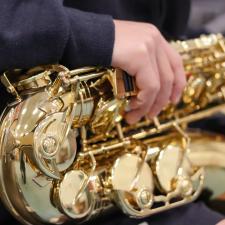 Saxophone resting on the lap of, with hands holding it. 